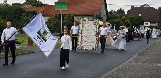 Die Spitze des Umzugs mit Ortswappen auf einer Fahne und einer Schautafel, die die Ersterwähungen auflistet.