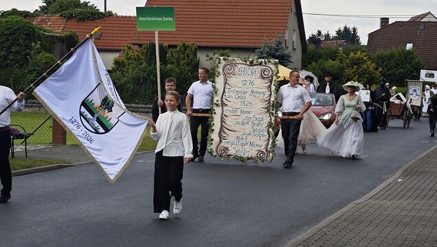 Die Spitze des Umzugs mit Ortswappen auf einer Fahne und einer Schautafel, die die Ersterwähungen auflistet.