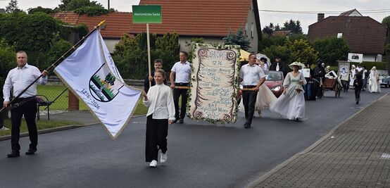 Die Spitze des Umzugs mit Ortswappen auf einer Fahne und einer Schautafel, die die Ersterwähungen auflistet.