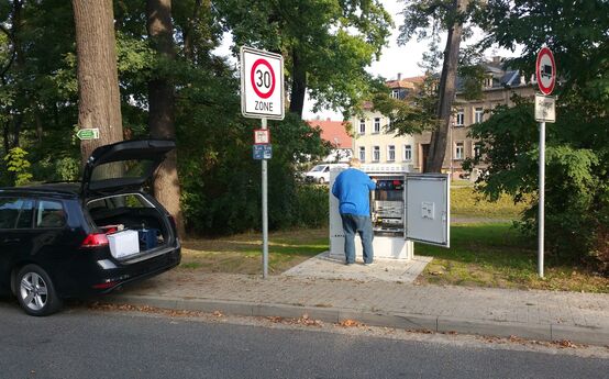 Ein Monteur vor dem ENSO-Multifunktionsgehäuse. Er stellt die Verbindung der VDSL-Vectoring-Technik der ENSO mit dem nahegelegenen Kabelverzweiger (KVz) der Telekom her. 